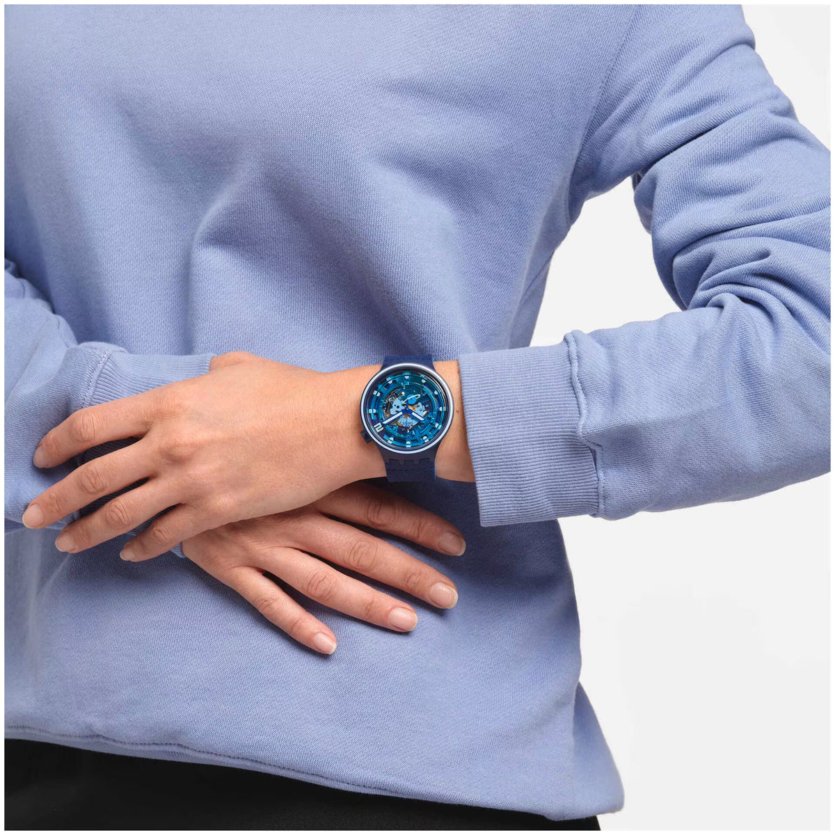 Blue silicone strap watch on wrist, round transparent dial with bold hour markers.