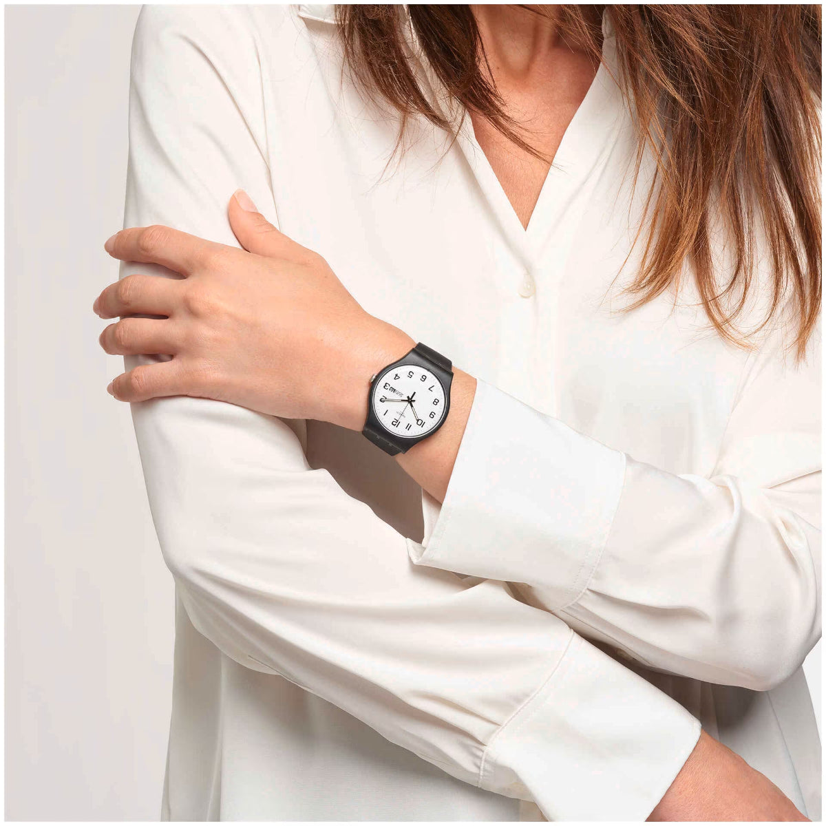 Unisex wristwatch on wrist with white dial and black strap, day/date text visible.