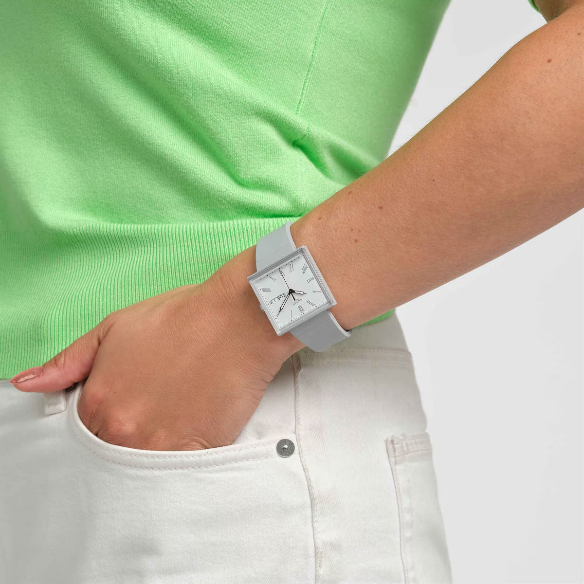 Square watch with white dial and gray strap, worn on wrist with cuff detail