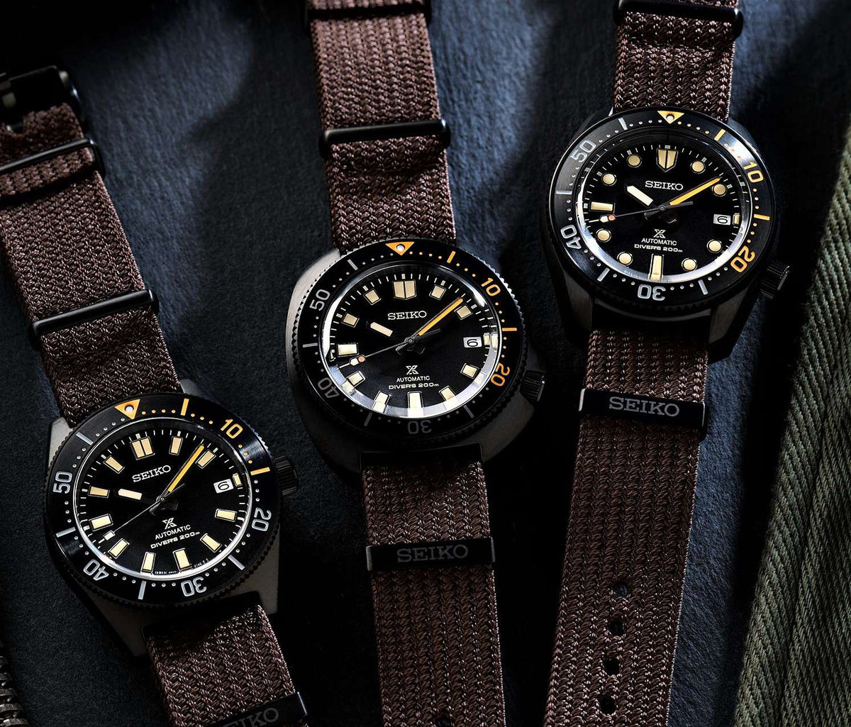Three black dive watches with brown textile straps and glowing gold markers
