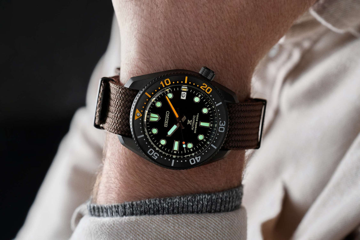 Seiko men's wristwatch on wrist with black dial and brown textile strap, green accents