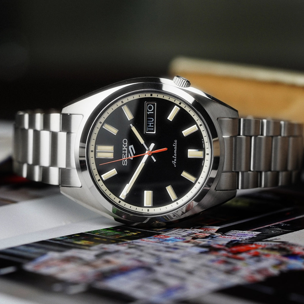 Seiko 5 Sports SNXS SRPK89K1 automatic watch resting horizontally on top of a colorful printed magazine.