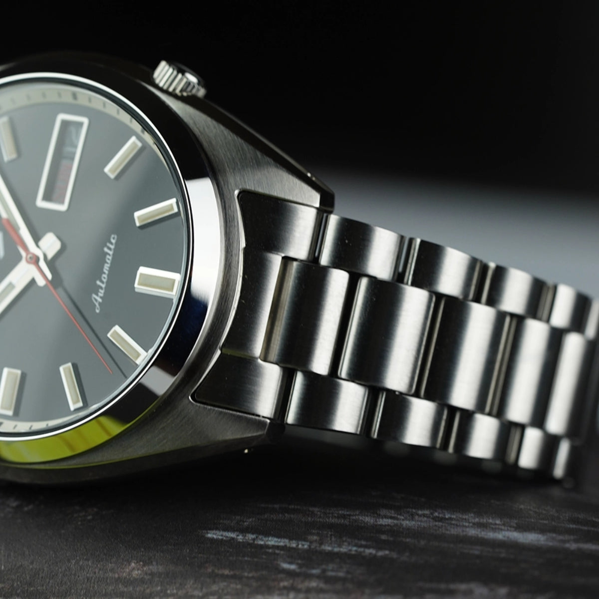 Close-up focusing on where the stainless steel bracelet integrates into the curved lug of the SNXS Seiko 5 wristwatch.