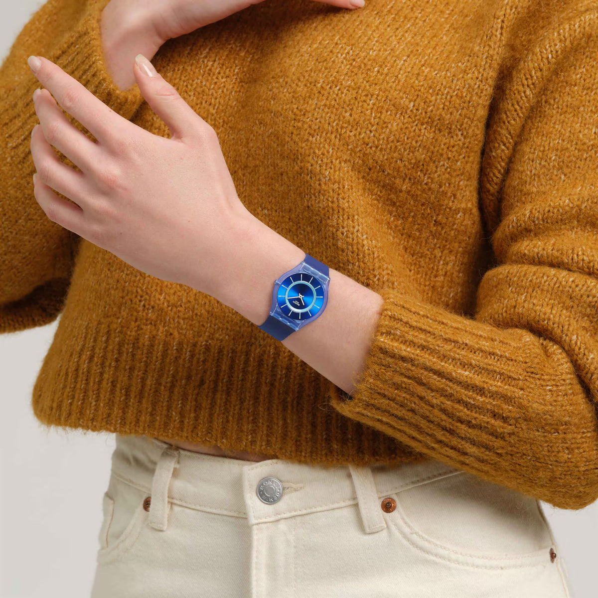 Blue silicone strap Swatch watch on wrist with blue dial, white markers, and slim case