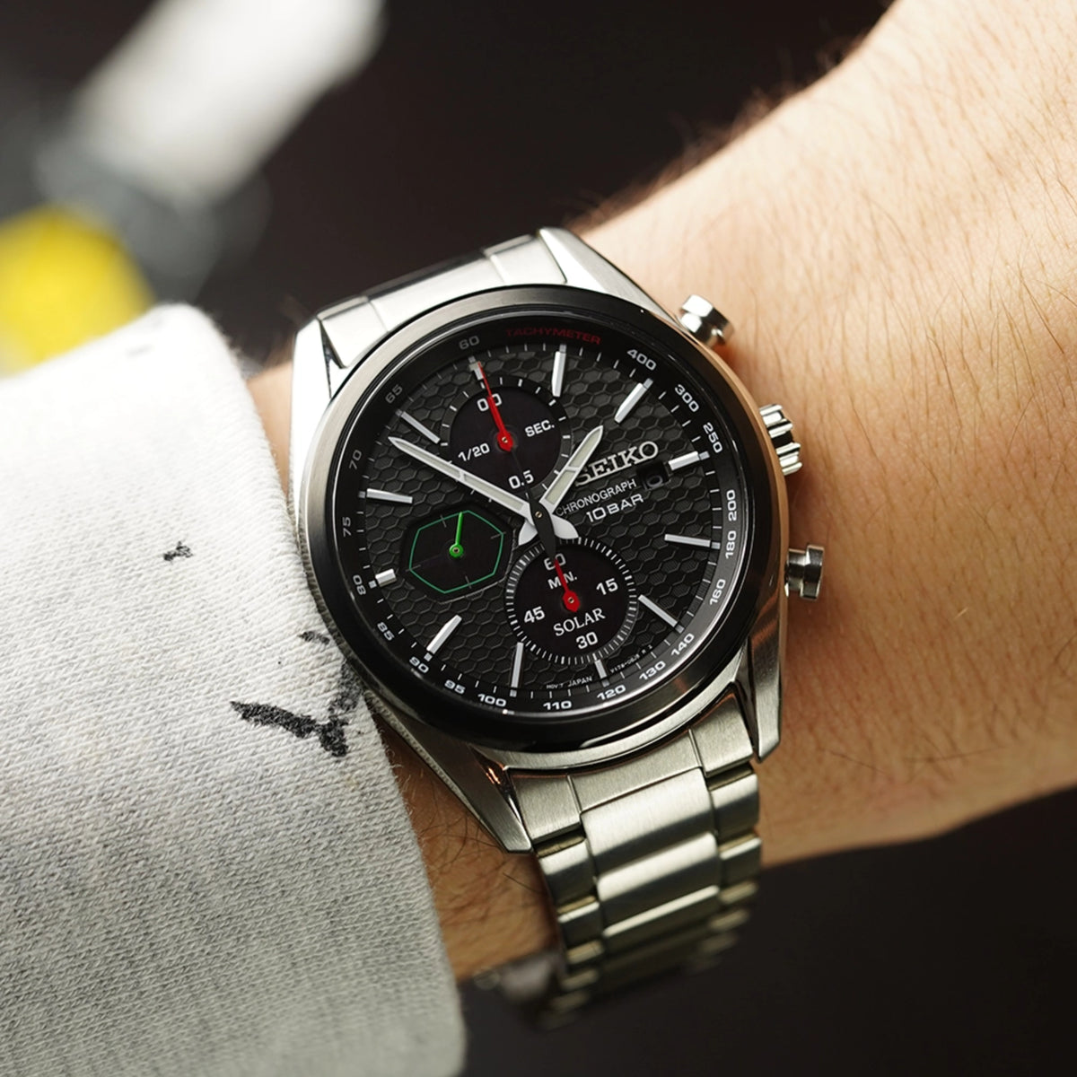 Seiko solar chronograph watch on wrist, black dial with green accents, steel bracelet