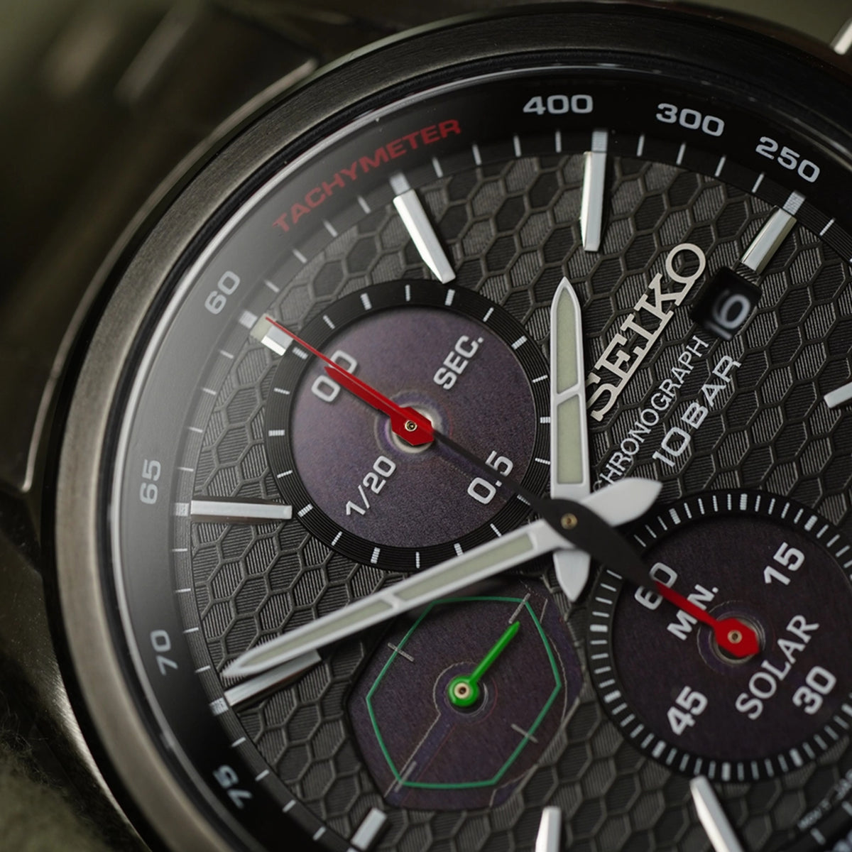 Solar chronograph close-up: black honeycomb dial, red tachymeter ring, subdials