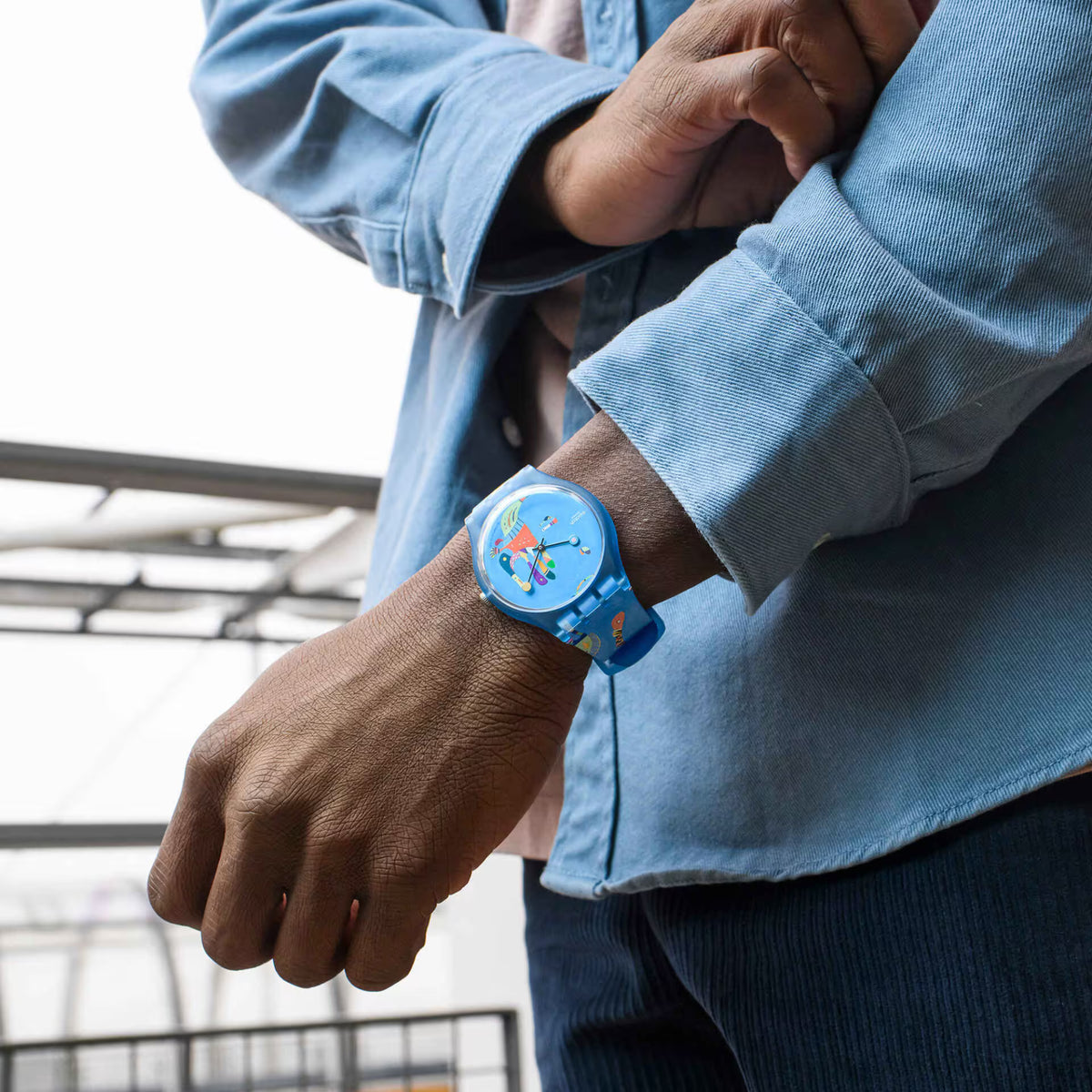 Blue silicone wristwatch on a wrist with light-blue dial and colorful artwork
