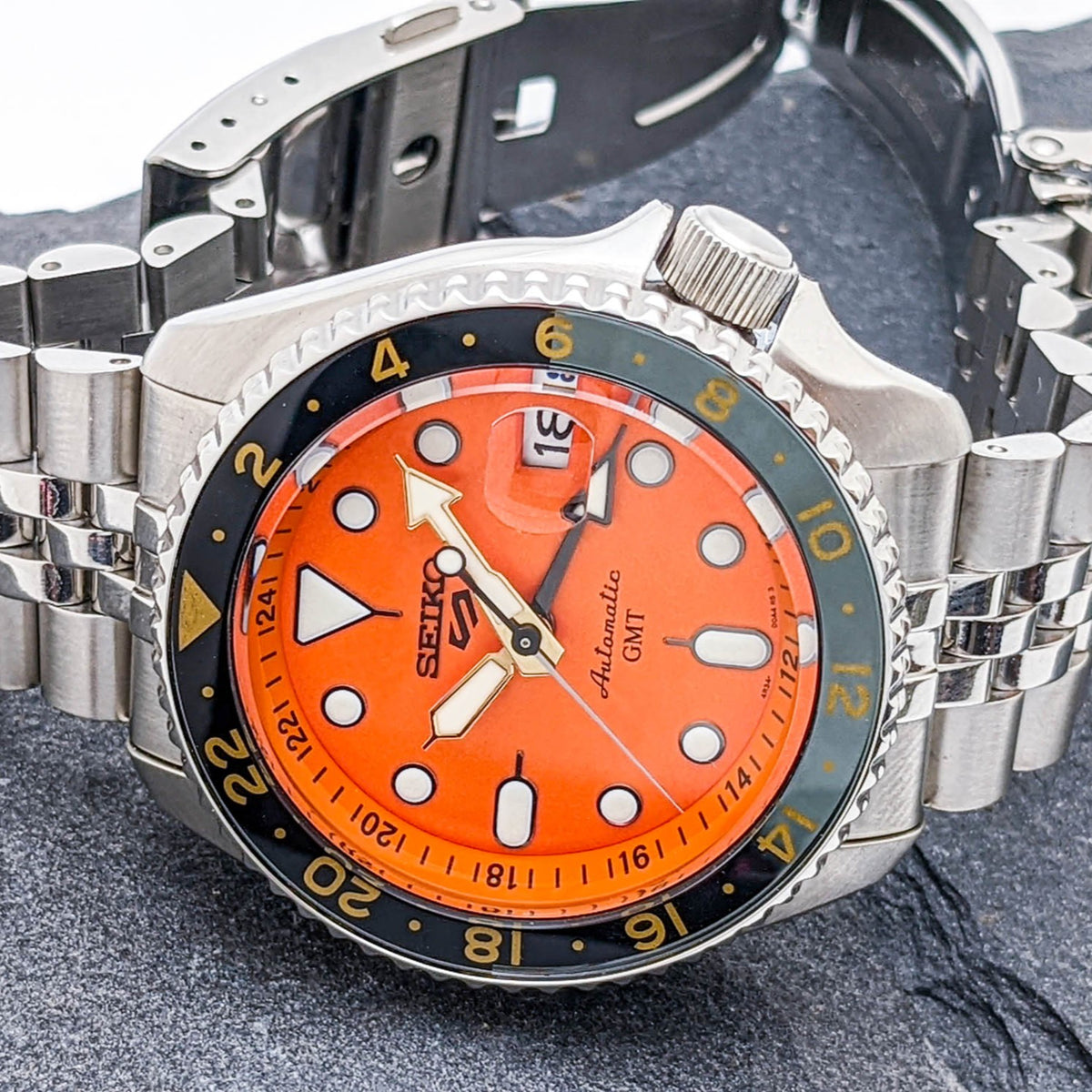 Men's Seiko GMT watch with orange dial, GMT bezel, and stainless-steel bracelet