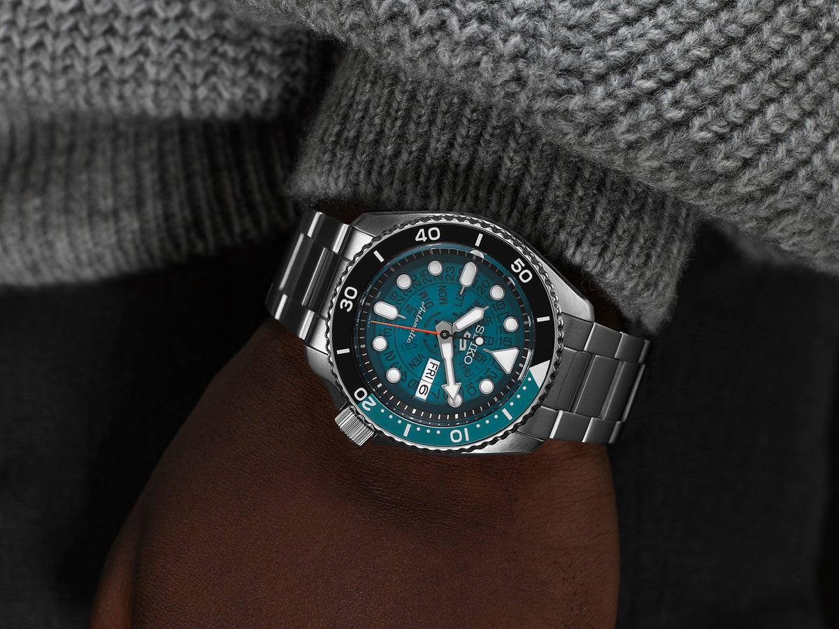 Men’s automatic watch on wrist with blue dial, black bezel, and steel bracelet