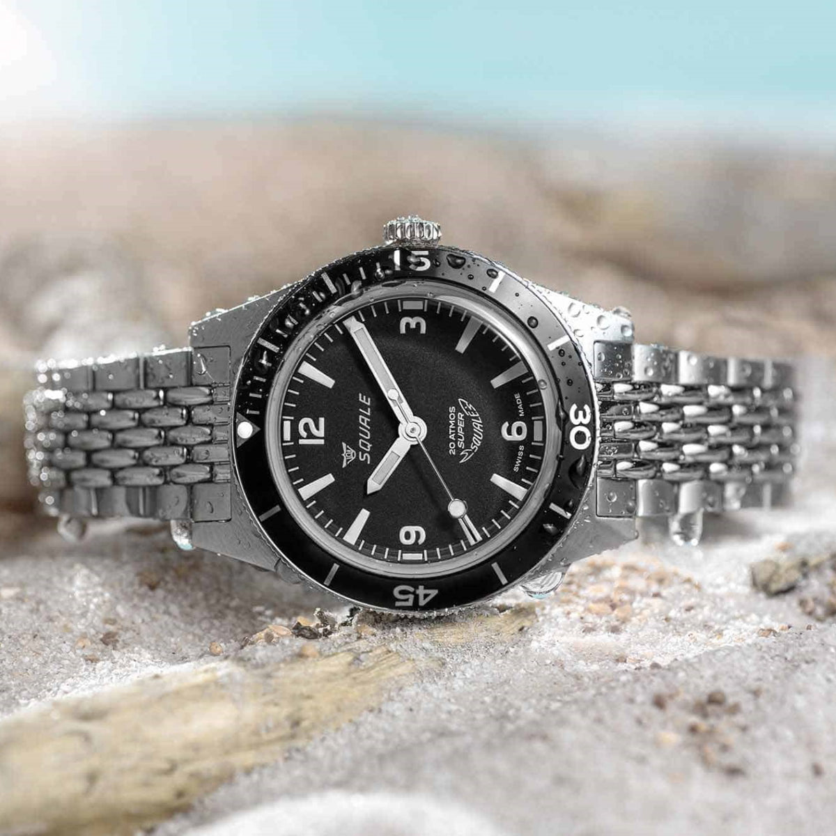 Squale Sub-30 Super Squale 20 Atmos dive watch with black dial and beads-of-rice steel bracelet resting on wet beach sand