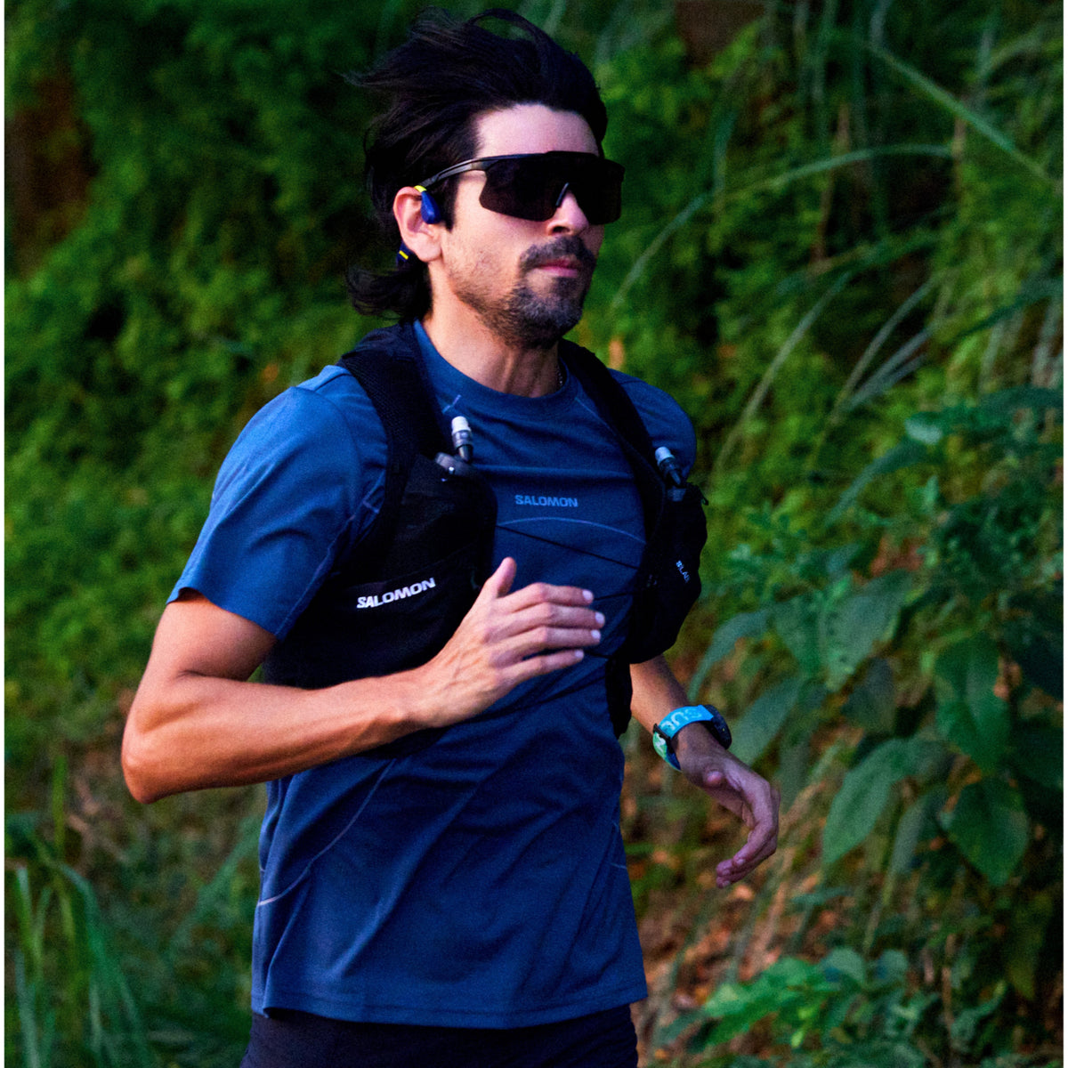 Male trail runner in sports vest wearing blue Suunto smartwatch and bone conduction headphones