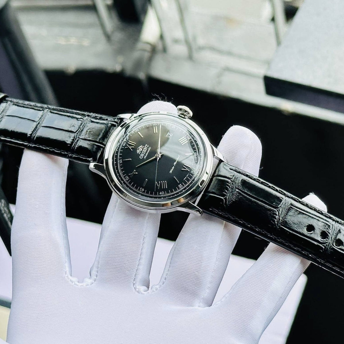 Automatic watch with black leather strap and black dial, worn over white gloves