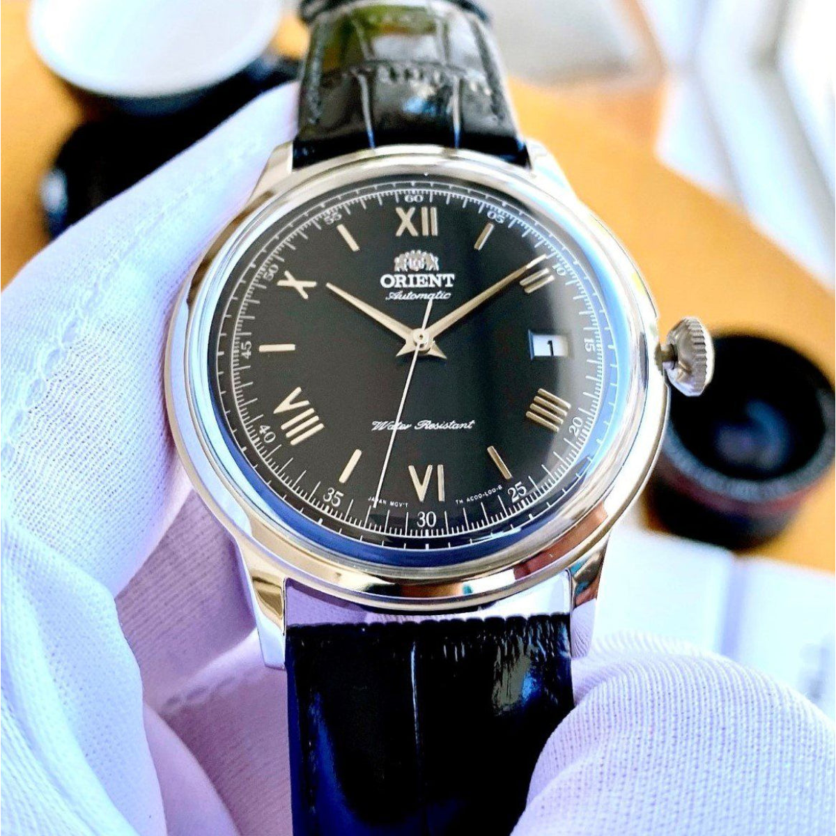Automatic watch with black dial, Roman numerals, and glossy black leather strap