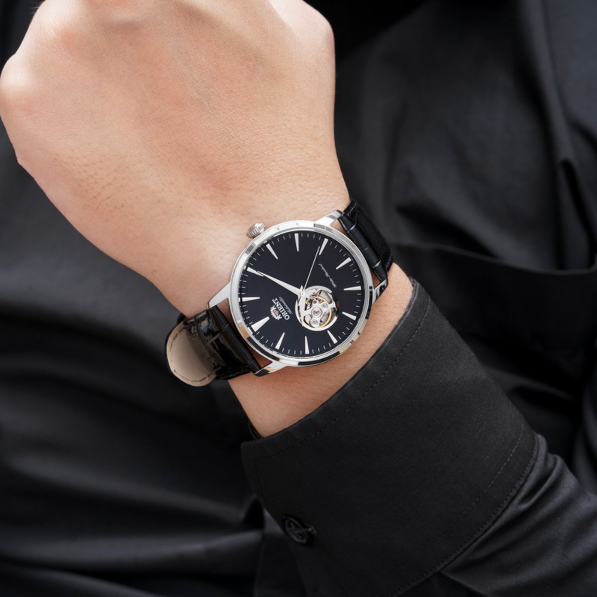 Orient automatic watch on wrist with black dial and open-heart skeleton movement; black leather strap