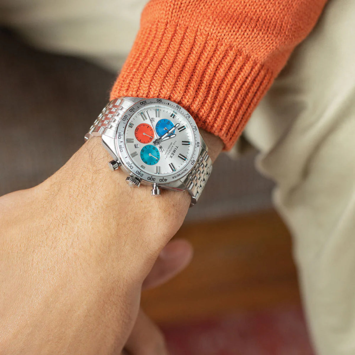 Men's chronograph quartz watch on wrist, silver bracelet and white dial, orange sleeve