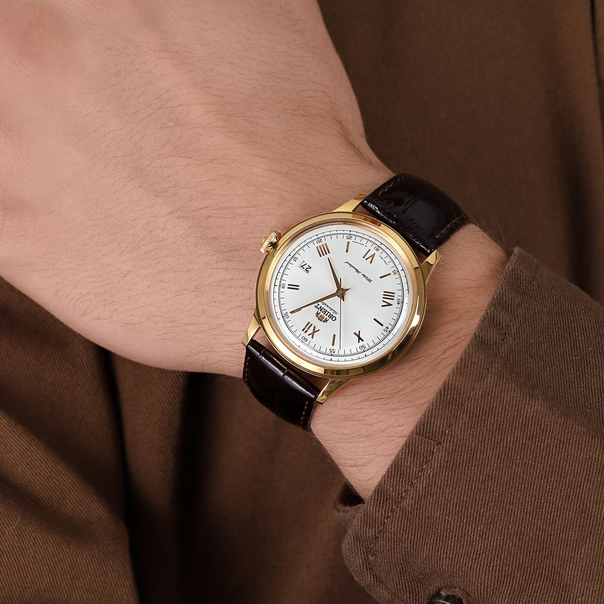 Men's automatic wristwatch on wrist with suit sleeve: gold-tone case, white dial, black strap