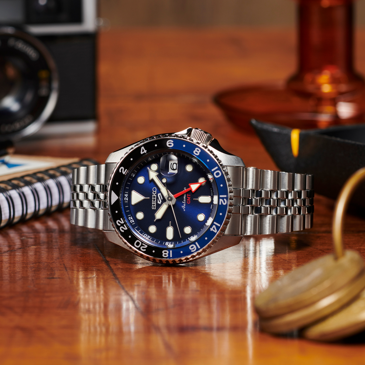 Stainless steel GMT automatic watch with blue dial, red accents, and metal bracelet