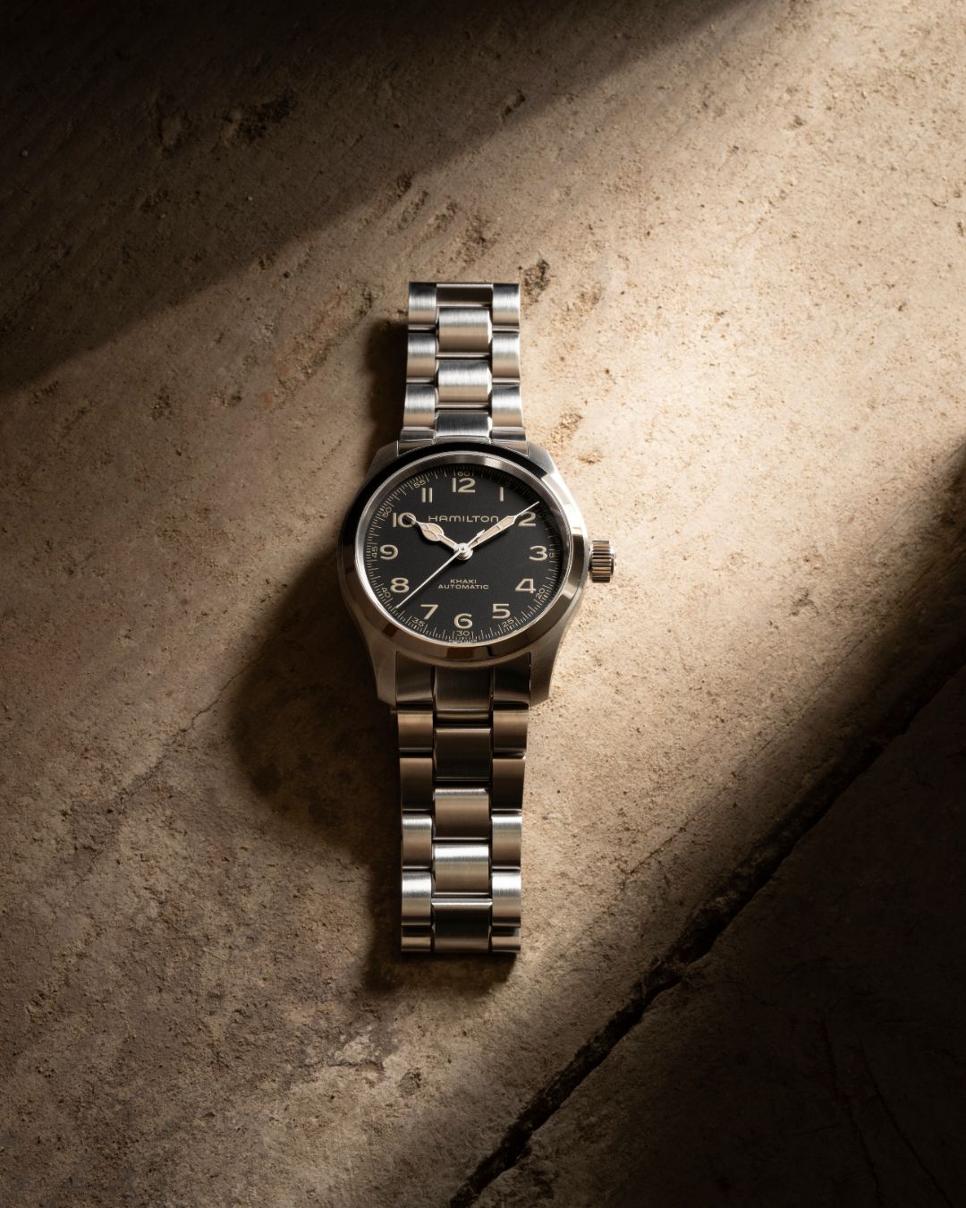 Hamilton Khaki Field Automatic watch with black dial and stainless steel bracelet resting on sunlit stone