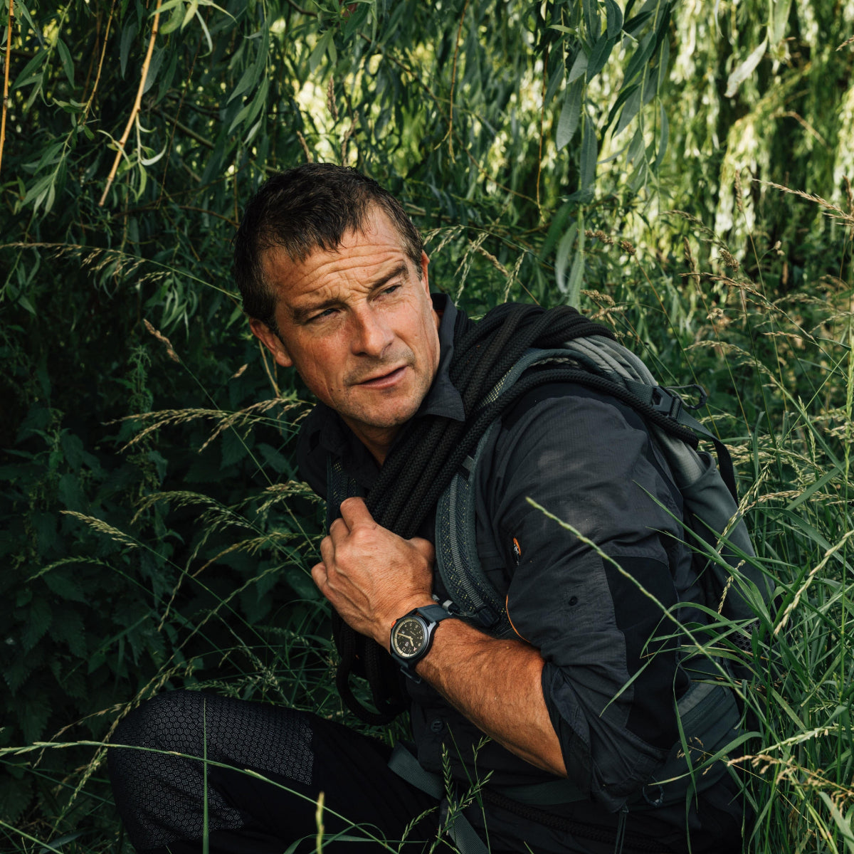Bear Grylls crouching in dense greenery wearing his signature Luminox Bear Grylls Survival XB.3716 adventure wristwatch