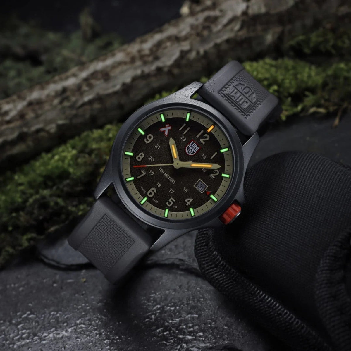 Angled view of the Luminox Bear Grylls Survival XB.3716 showing illuminated tritium tubes glowing green and orange in dark surroundings