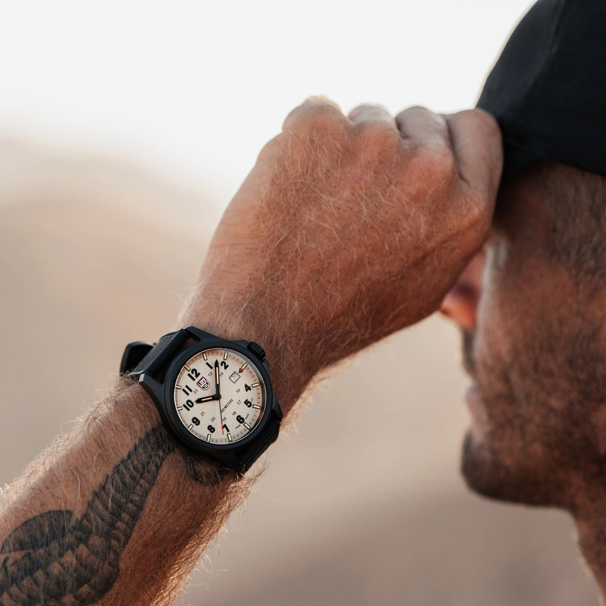 Grey dial field watch with black case and textured fabric strap, luminous hour markers