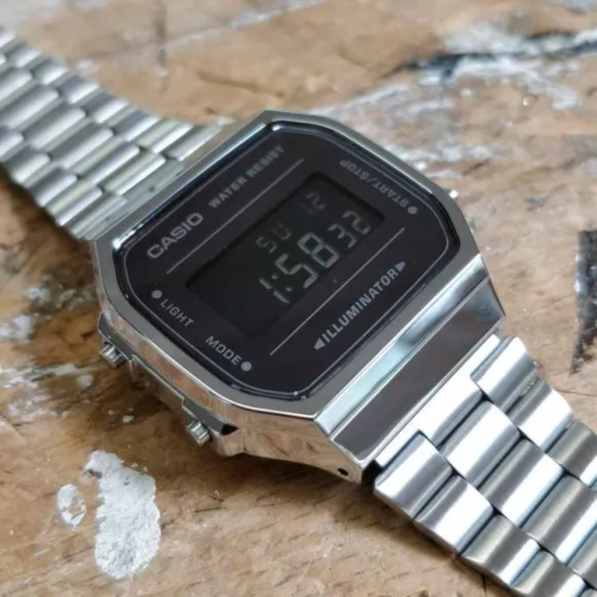 Angled close-up of the Casio Vintage Retro A168WEM-1EF quartz watch resting on a rustic wooden surface, highlighting its chrome-plated case