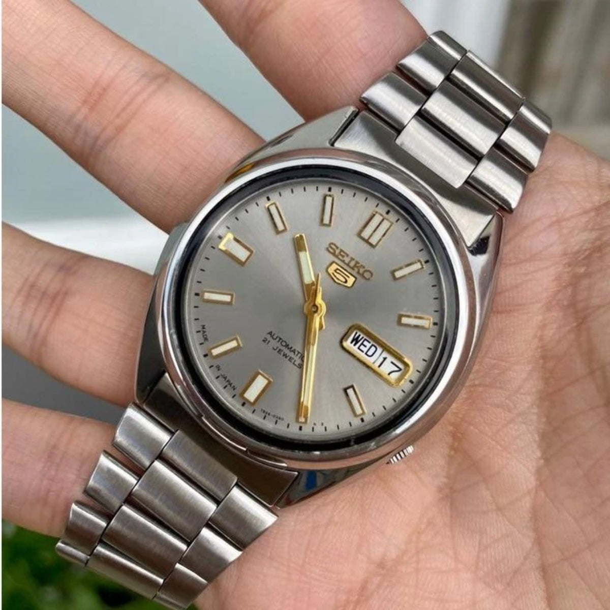 Seiko 5 automatic watch SNXS75K1 close-up with light grey dial, gold hands, steel bracelet, date window