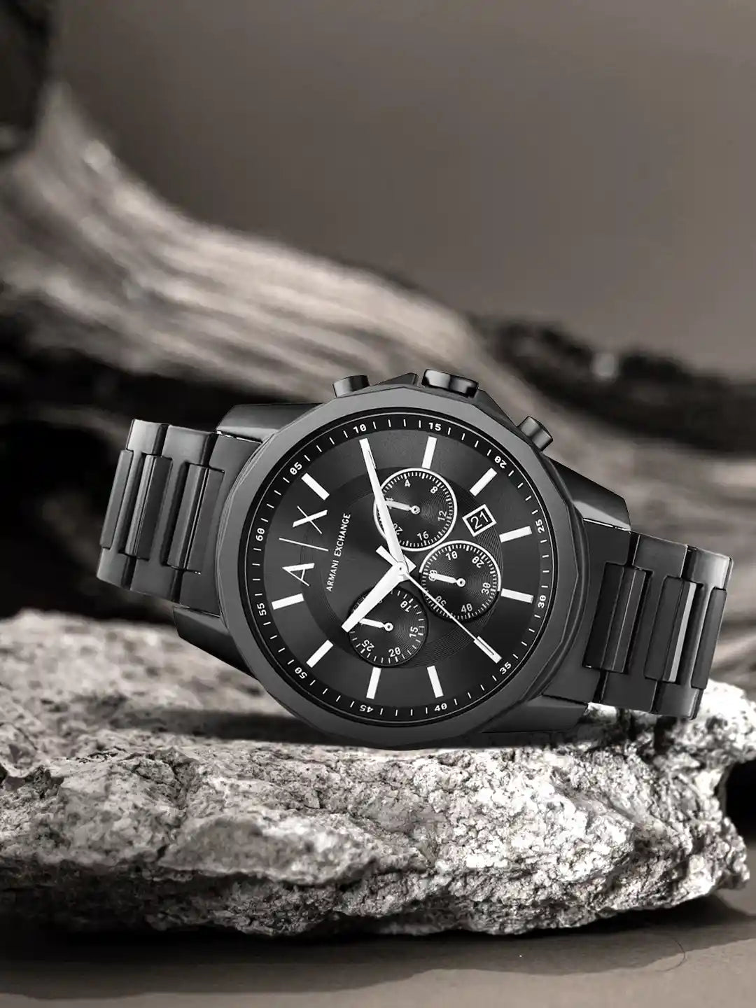 Armani Exchange black stainless steel men's chronograph watch resting on a rugged grey stone surface
