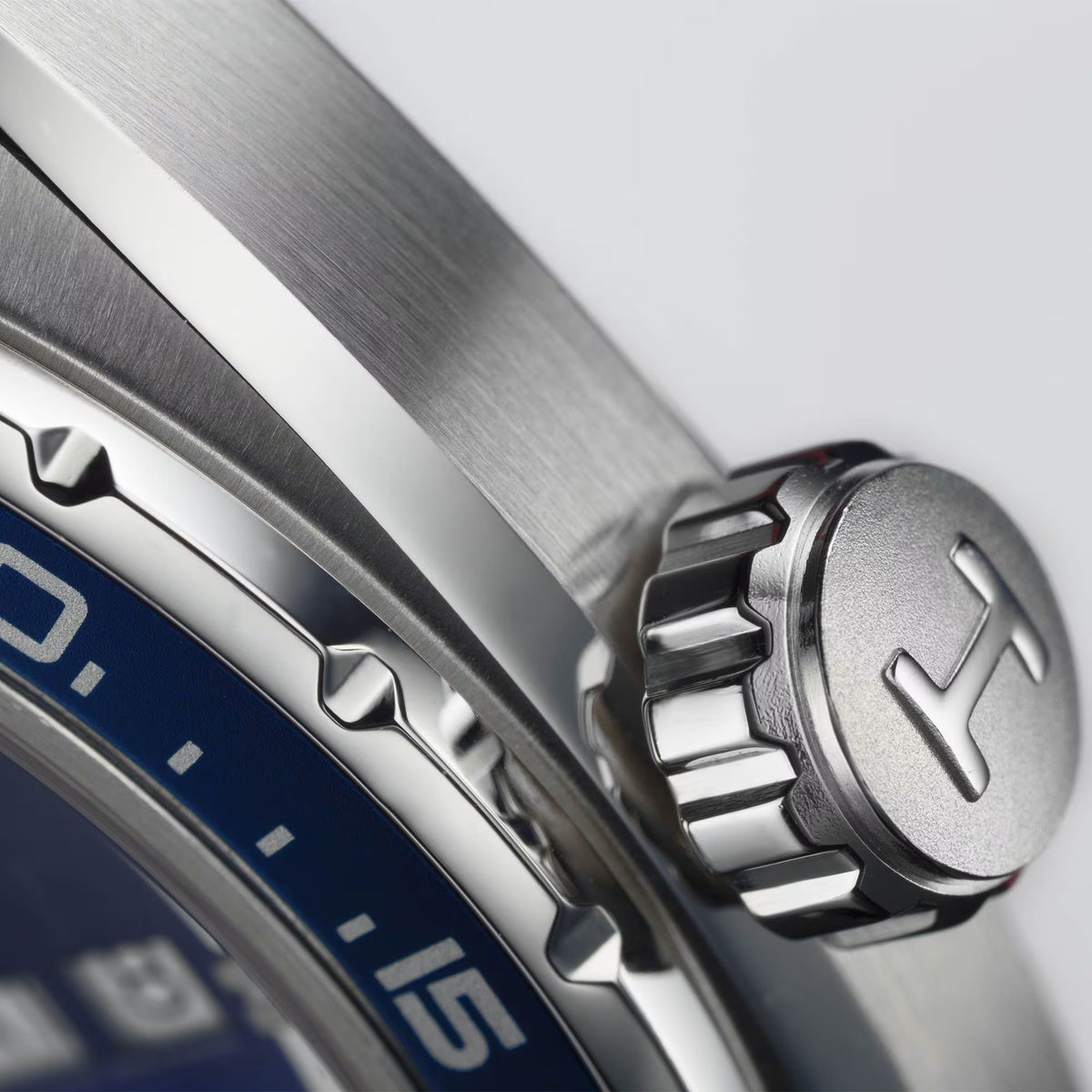 Extreme close-up of a Hamilton watch crown engraved with the brand's signature "H" logo