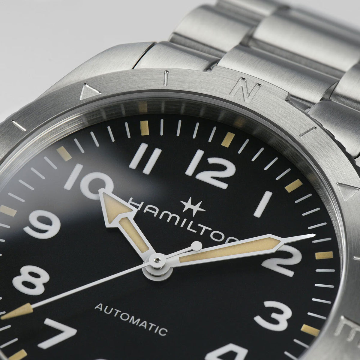 Close-up of a Hamilton automatic watch with a black dial, white numerals, and beige arrow hands under a brushed steel bezel