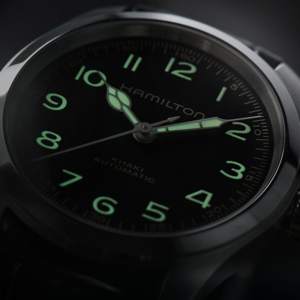 Hamilton Khaki Field Murph H70405730 watch macro view showcasing luminous hands and beige printed numerals on black dial in low light