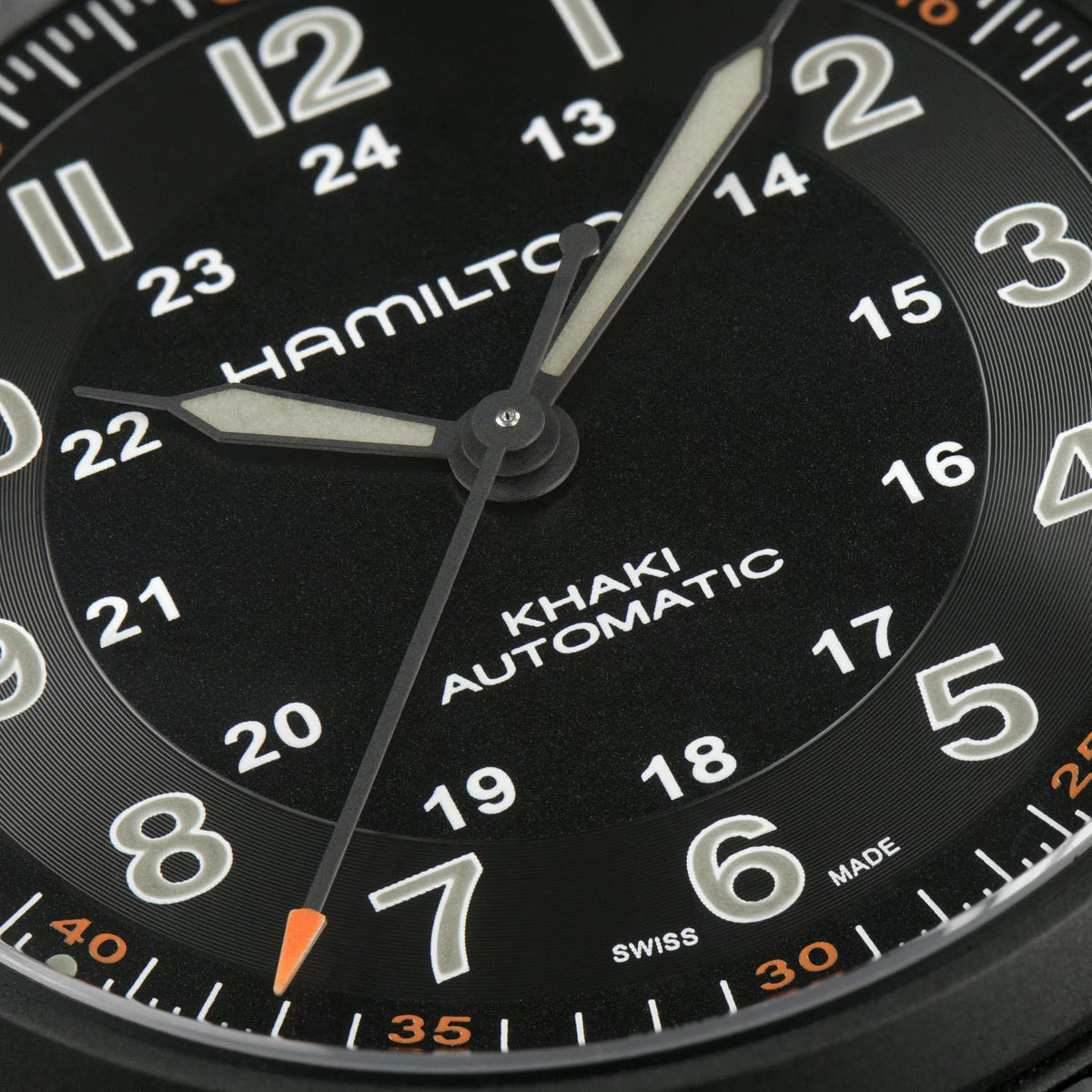 Close-up of black watch dial with Hamilton branding, numerals, and automatic hands
