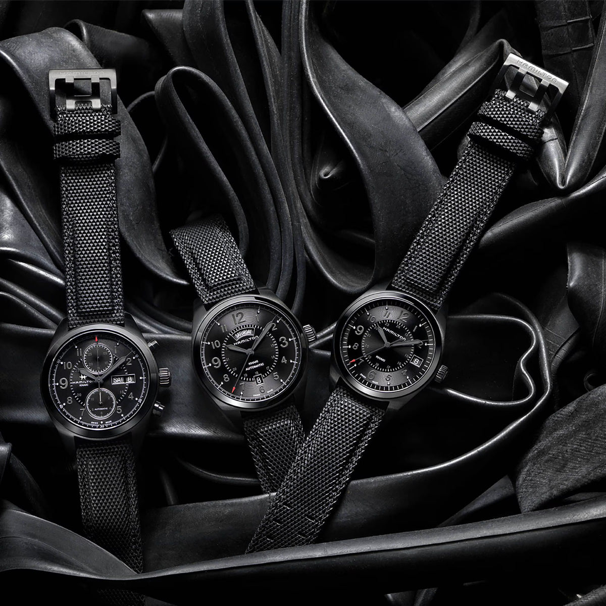 Hamilton Khaki Field H71626735 brand collection layout showing three all-black field watch models resting on a dark, textured background