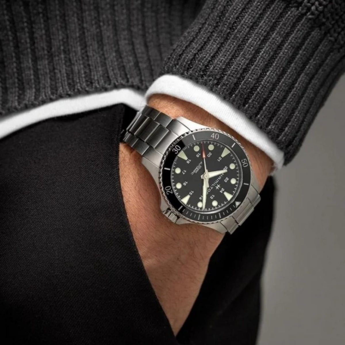 Hamilton Khaki Navy H82335131 mens Swiss timepiece styled on the wrist with a dark grey jumper and black trousers