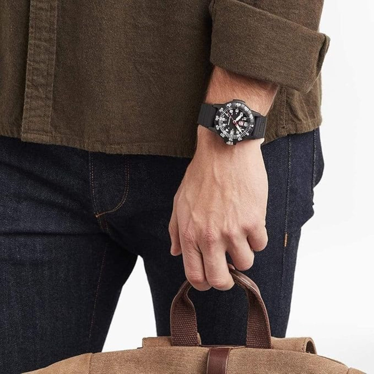 Men's wristwatch with black dial and silicone strap on a hand holding a brown bag