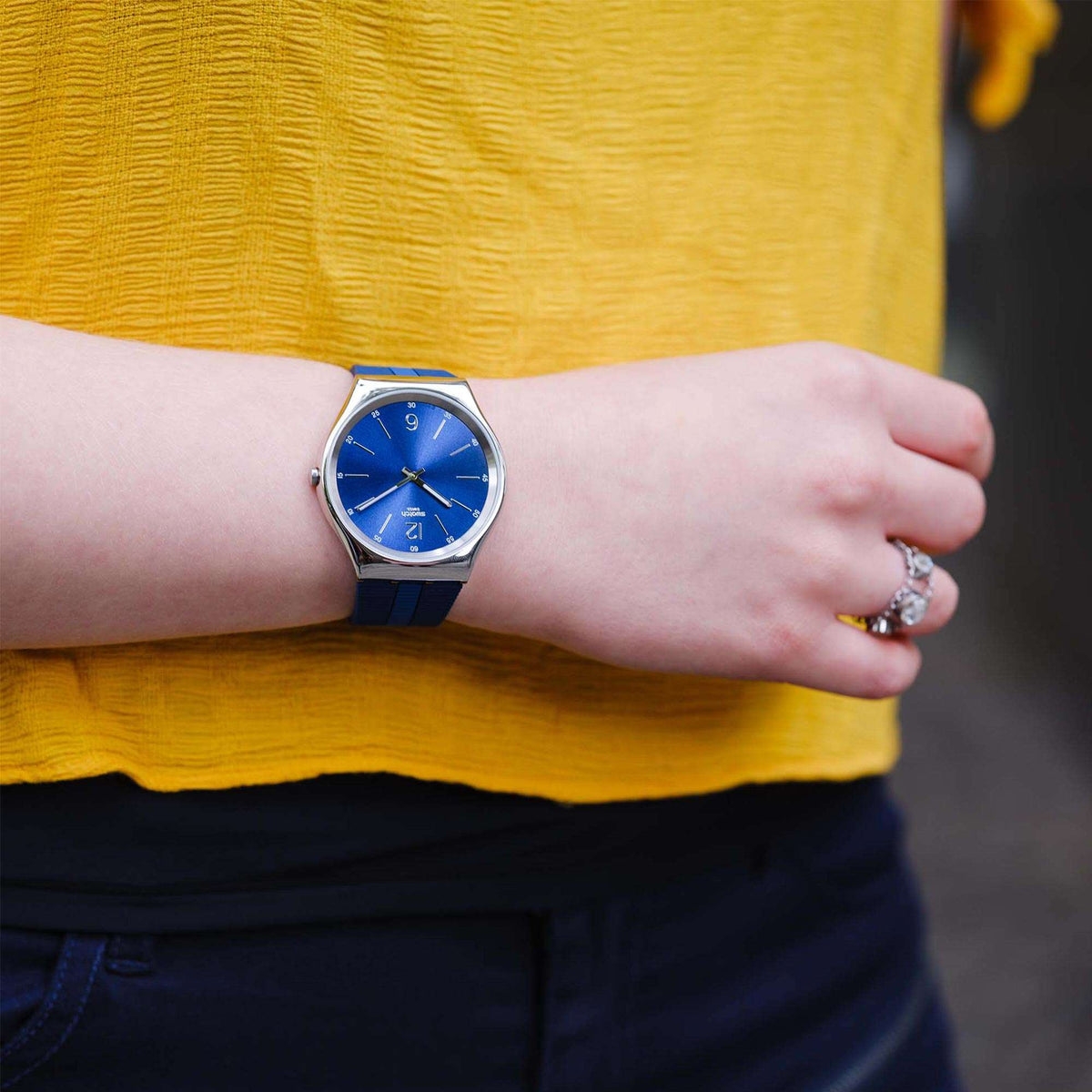 Blue-dial Swatch quartz watch on wrist with blue rubber strap and silver case.
