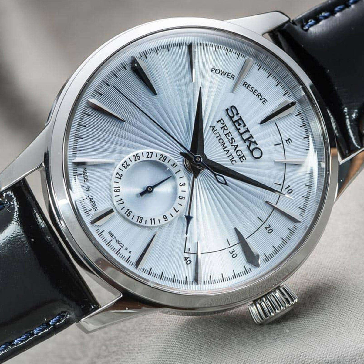 Men's automatic watch dial close-up, silver sunray texture with blue hour markers