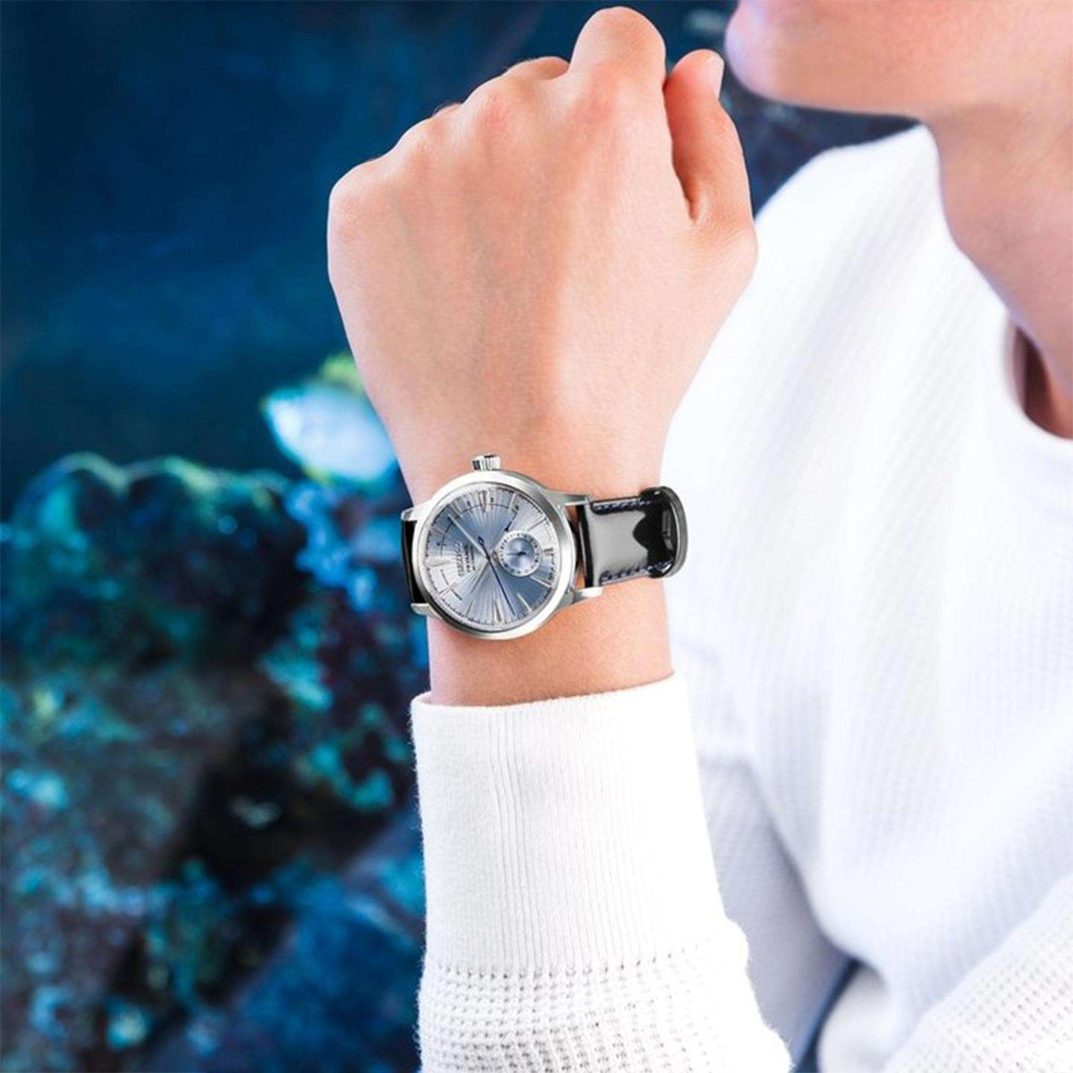 Men's automatic watch worn on arm, silver dial, black leather strap with blue stitching