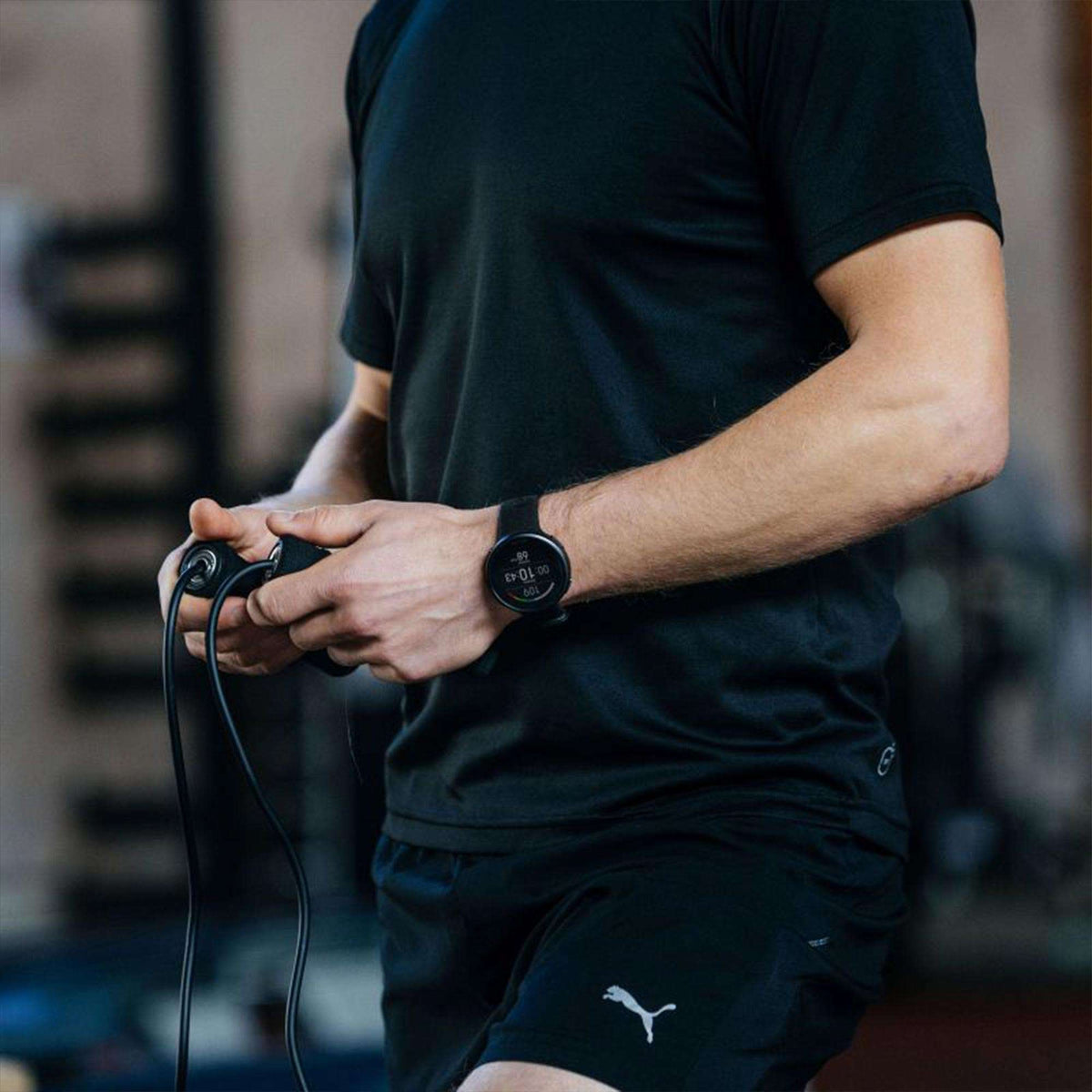 Black rubber-strap smartwatch on forearm, showing a round dark digital face
