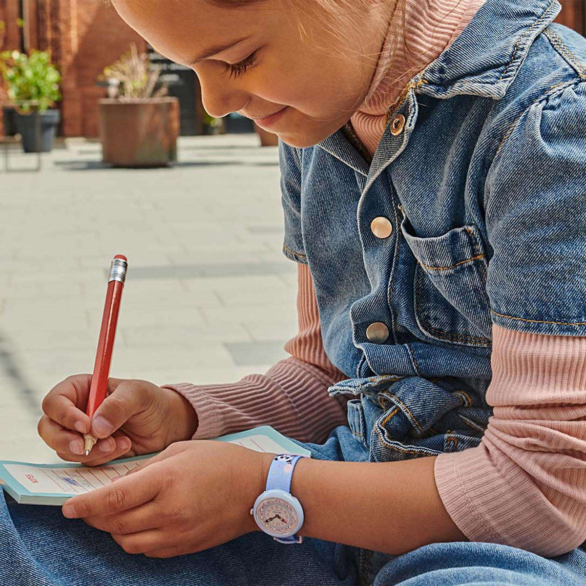 Kids wristwatch on arm: round light-blue case with pink dial and blue panda-print band