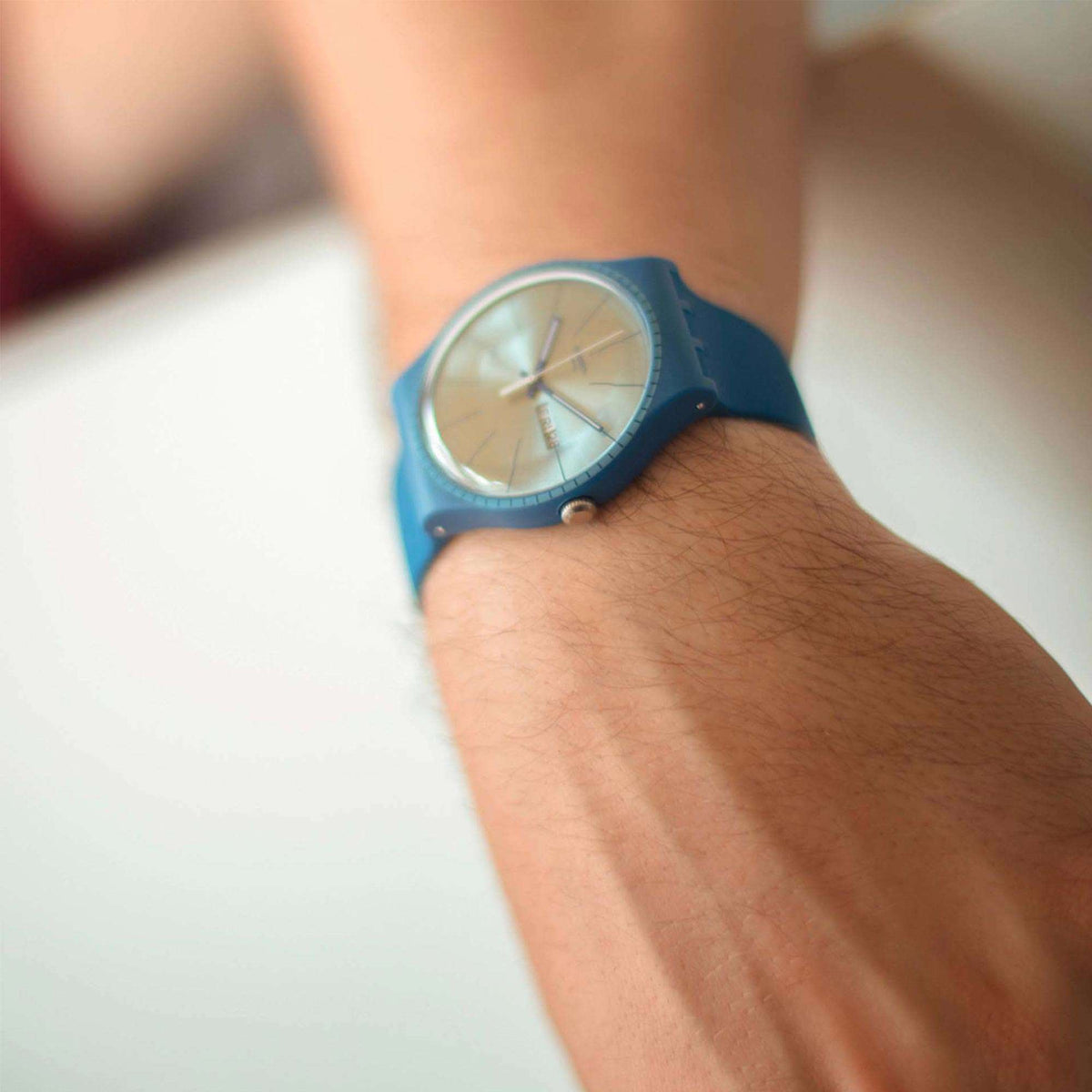 Men's blue silicone watch on wrist with silver dial, slim hands, and hour markers