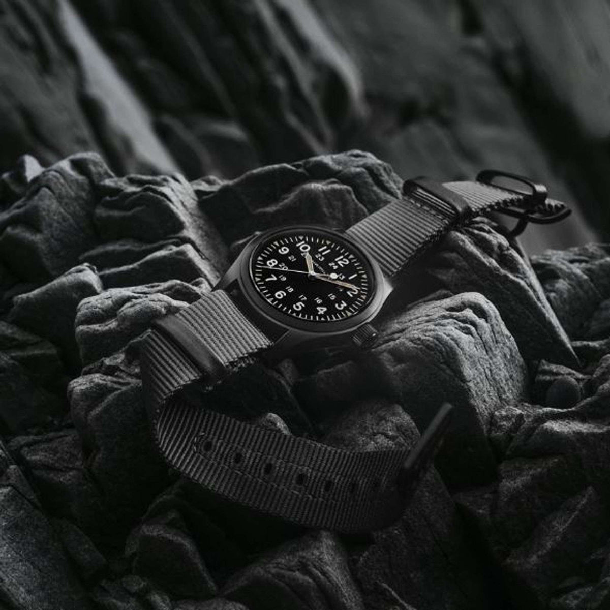 Hamilton Khaki Field Automatic watch with black dial and grey NATO strap resting on dark rocks