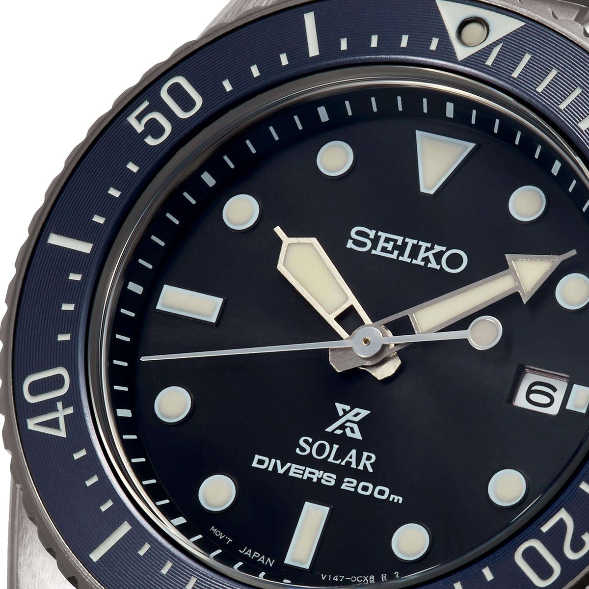 Solar diver watch close-up: dark dial with lume markers, Seiko text, blue bezel
