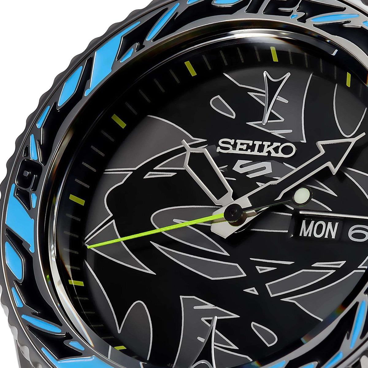 Close-up of black patterned watch dial with green accents, hands, and day/date window