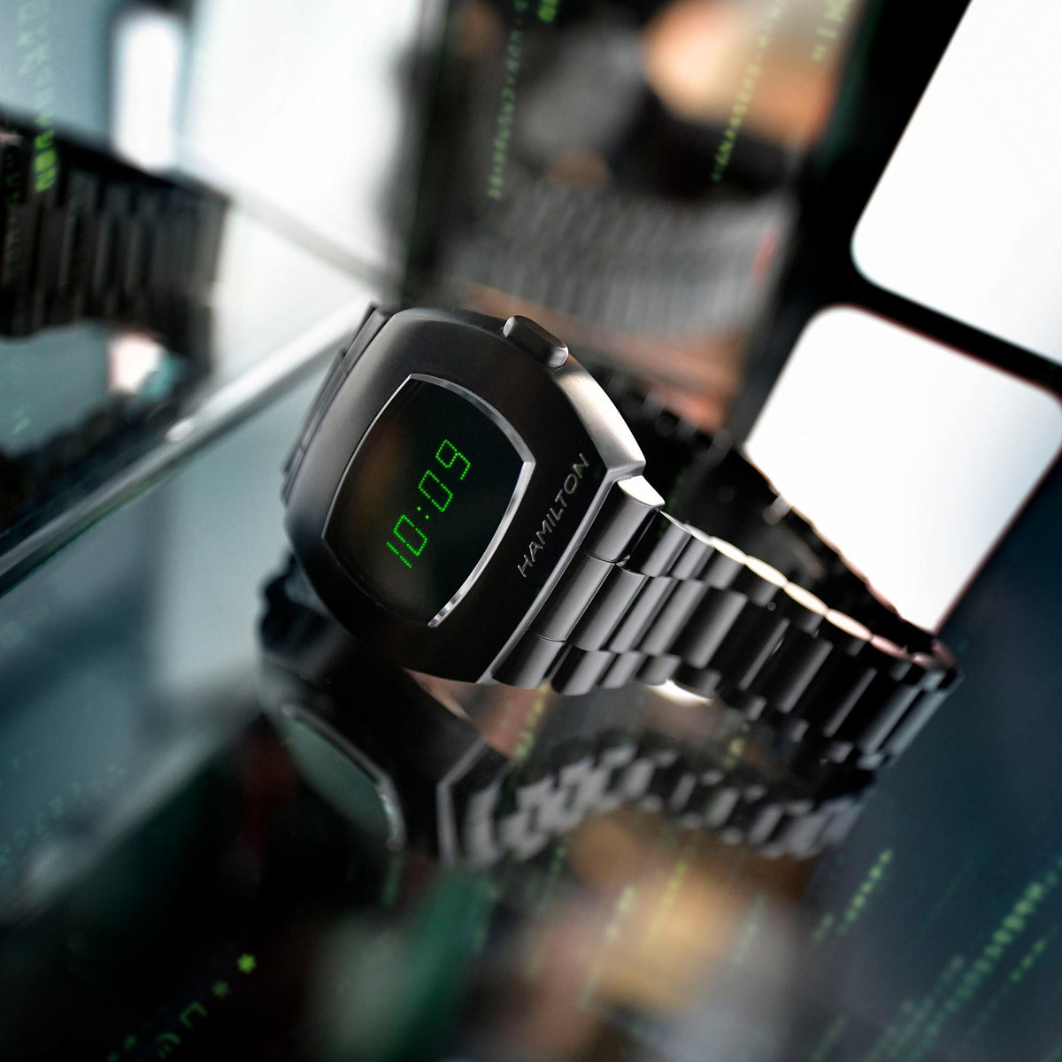 Close-up Hamilton men's watch with green digital time on dark LCD and metal bracelet