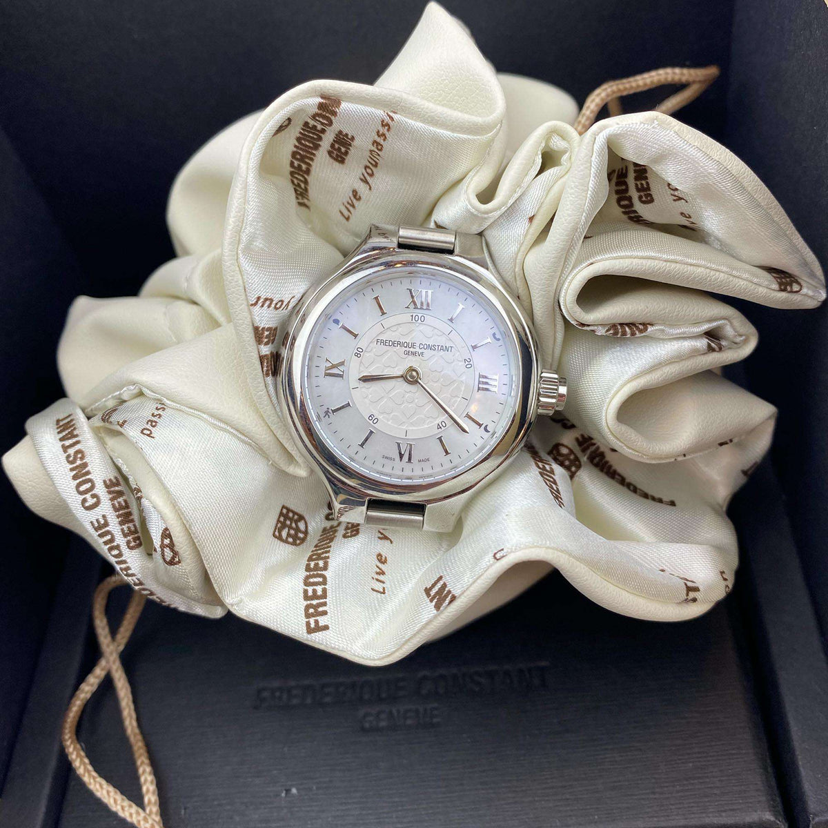 Stainless steel ladies wristwatch on cream cloth, with metal bracelet and crown
