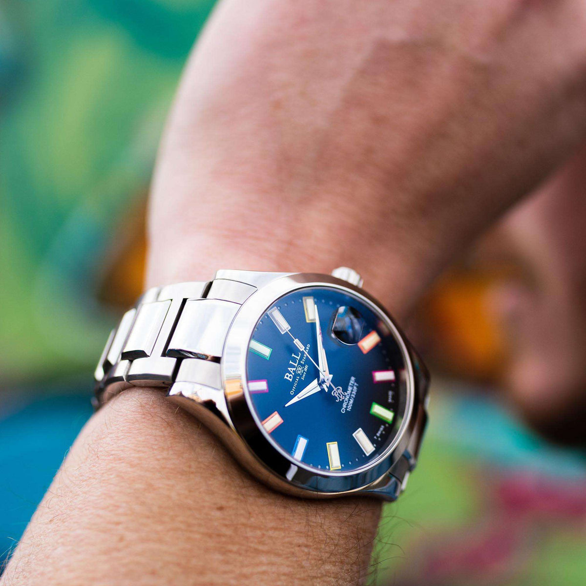 Men's wristwatch on hand with blue dial, multicolor markers, and round bezel