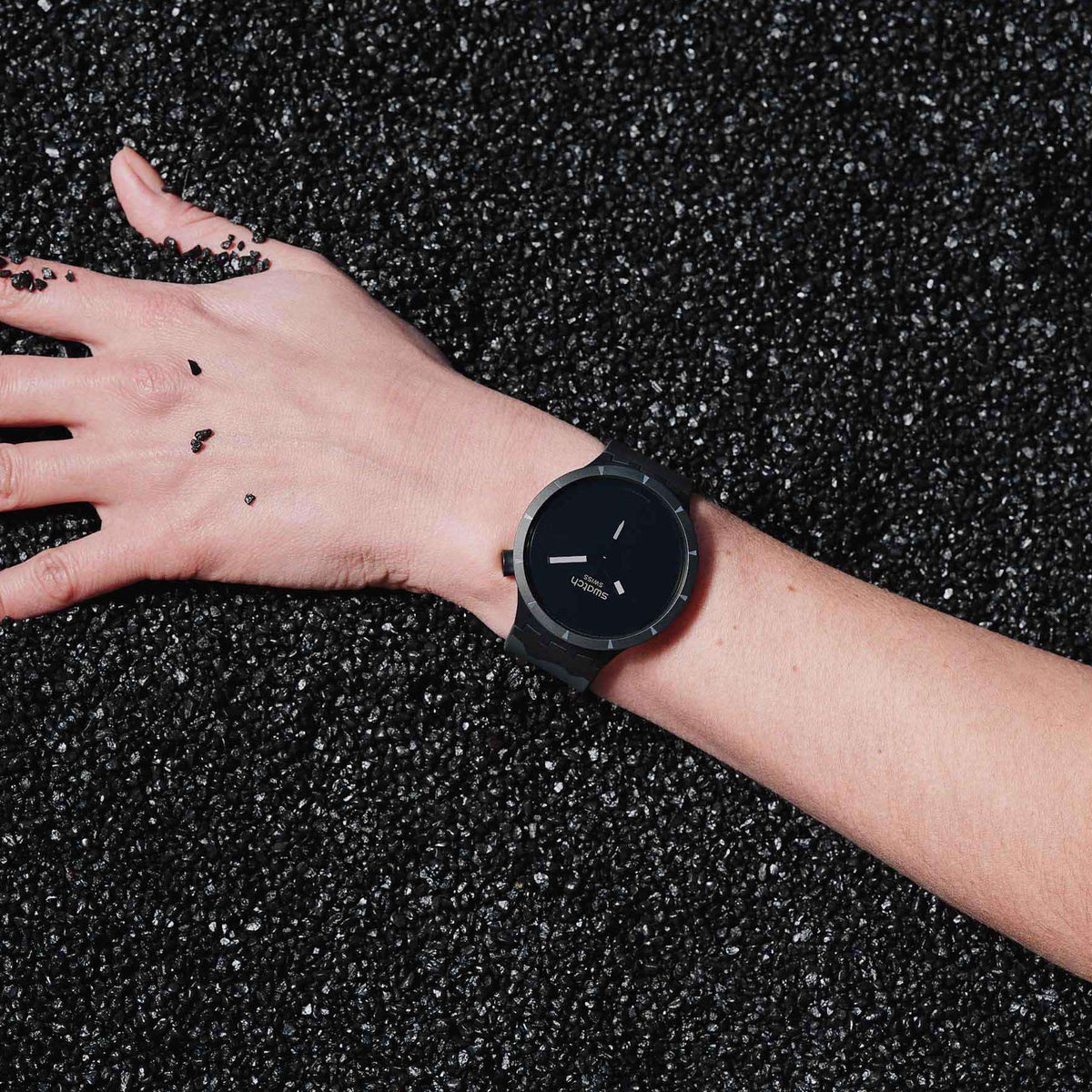 Black dial Swatch watch on wrist with silicone strap over textured dark ground