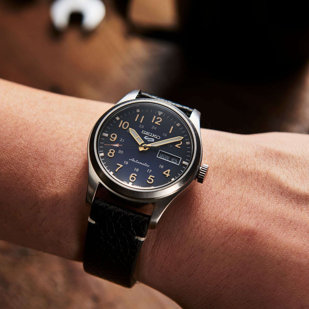 Men's automatic wristwatch worn on wrist, blue dial with date window, black leather strap