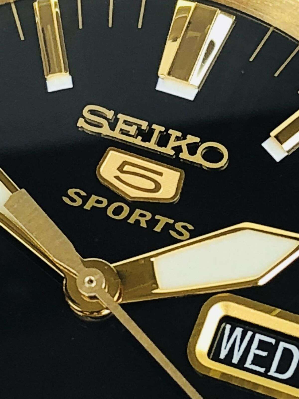 Seiko 5 Sports black dial close-up with logo, gold hands, and Wed date window